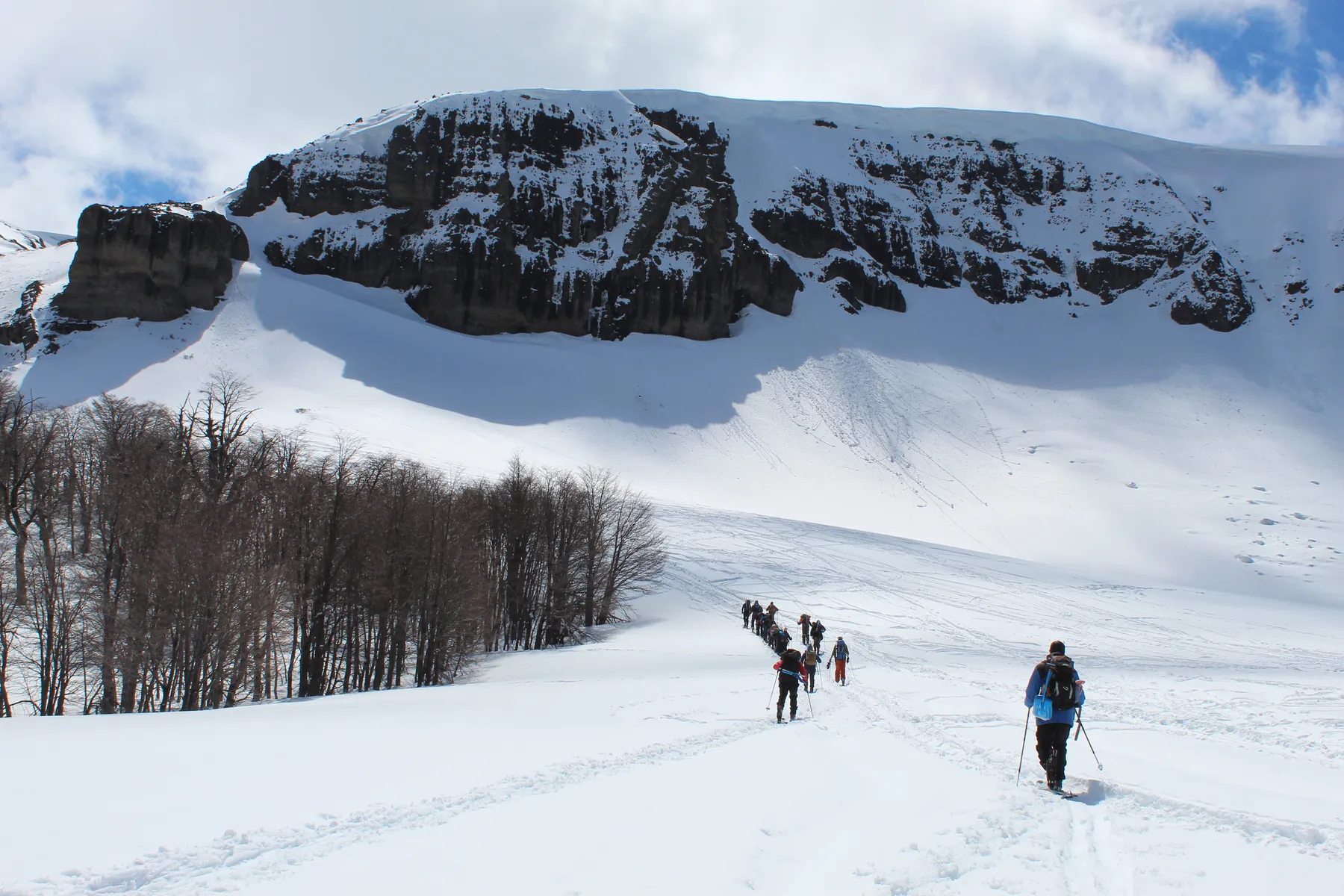 Grupo en randonnée bajo una pared volcánica nevada